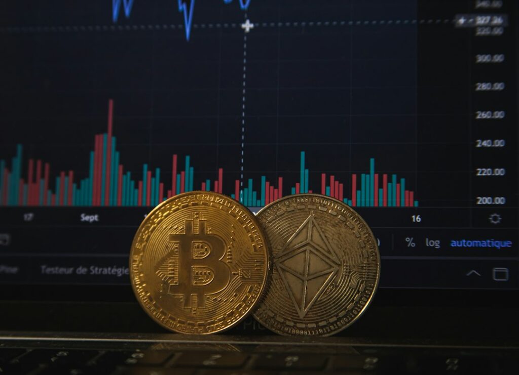 Bitcoin and Ethereum coins on laptop keyboard in front of trading chart