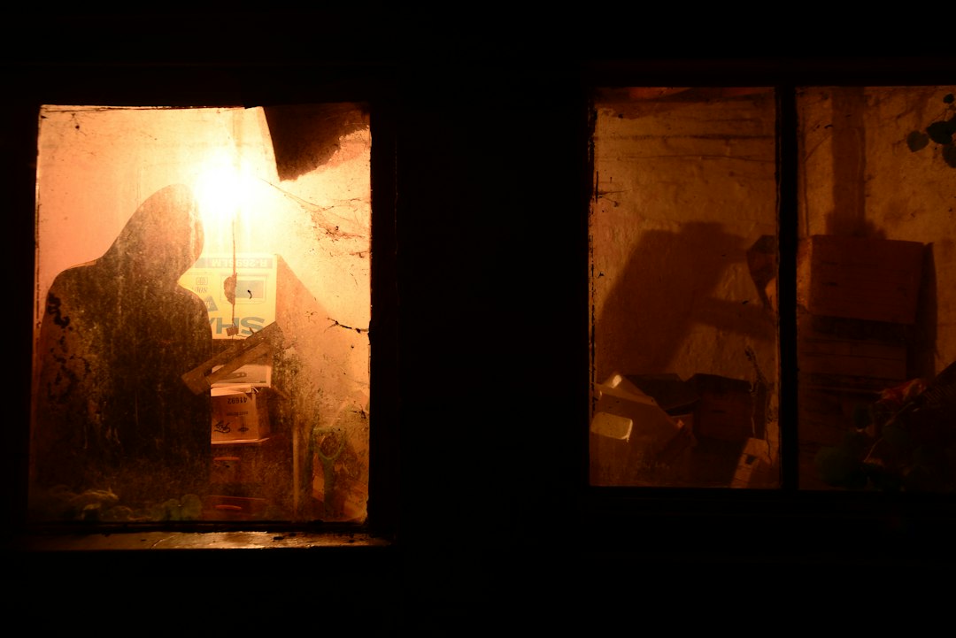 A dark figure standing by a window at night, evoking the threat of a home invasion